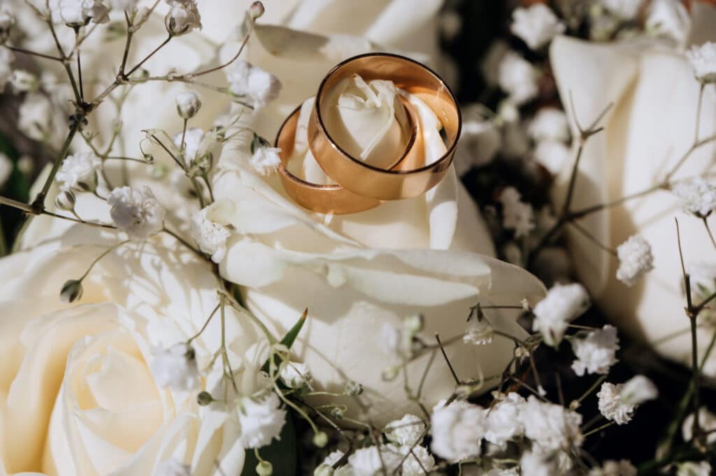 Golden wedding rings resting on a white rose surrounded by delicate baby's breath, symbolizing a happy marriage and eternal love.