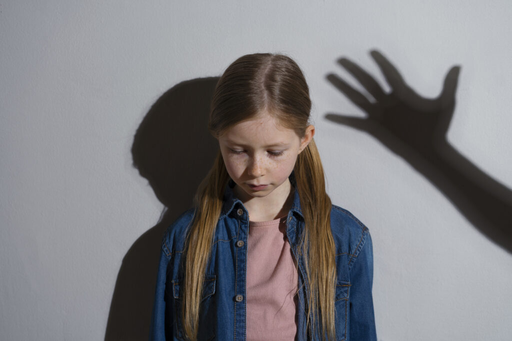 A young girl looking down with a shadow of a raised hand, symbolizing the challenges of spanking needs in parenting.