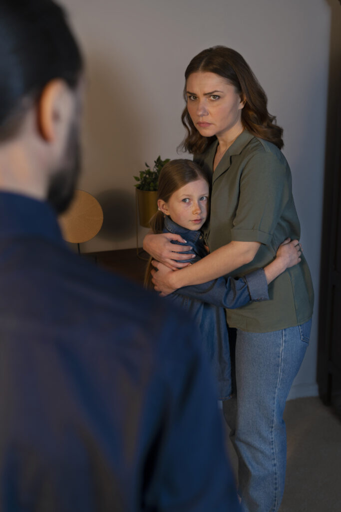  A worried mother holding her daughter closely, looking sternly at a man in the foreground, illustrating the emotional toll of what happens if you discipline too much.