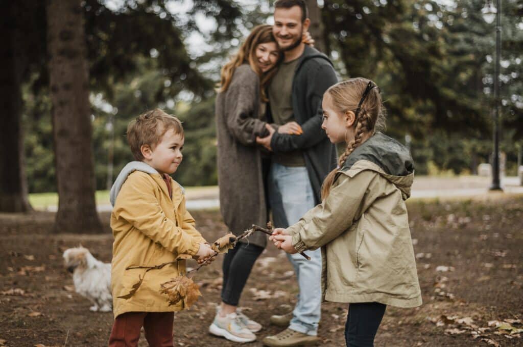 A happy family enjoying nature with two children playing together while the parents watch lovingly in the background, illustrating how guidance and advice can help kids develop positive social skills.