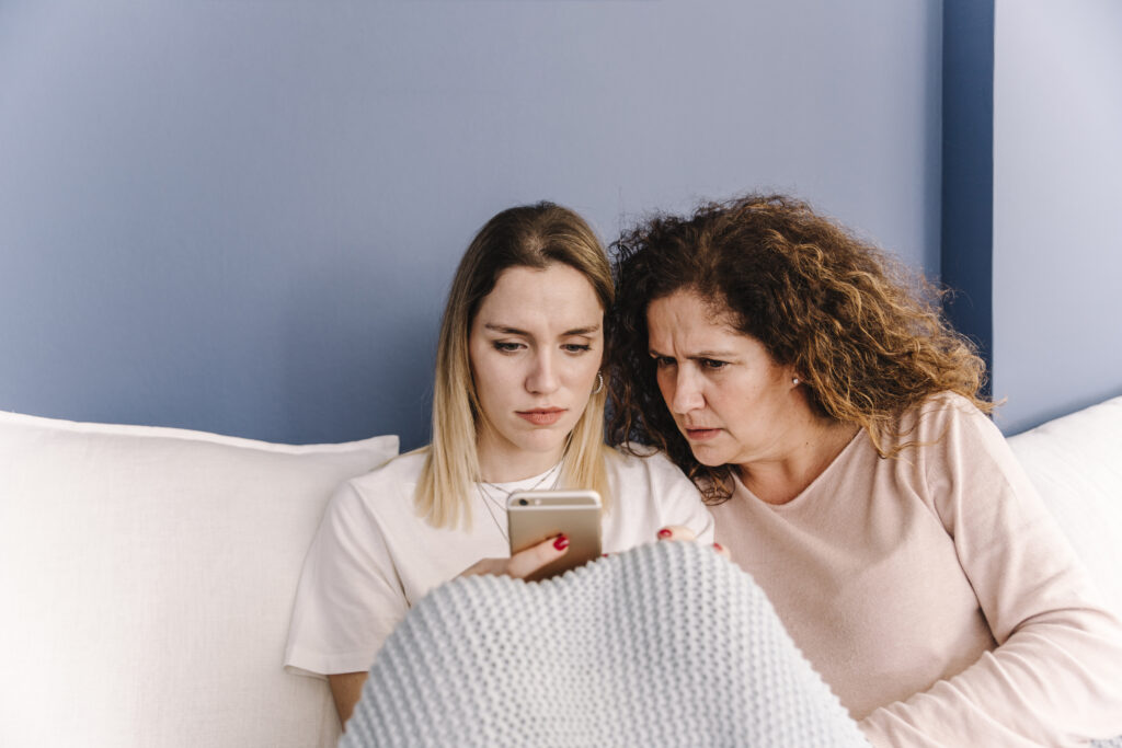 A mother and daughter intensely looking at a smartphone, reflecting the strained dynamics often experienced by those raised by a narcissist.