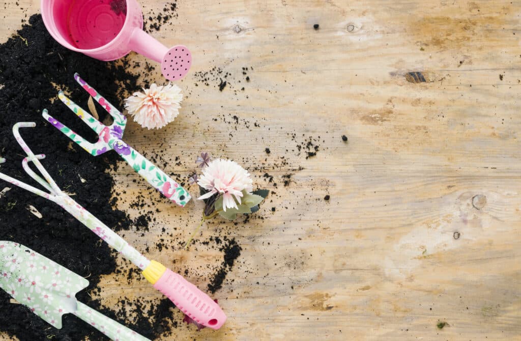 Colorful gardening tools, pink watering can, and scattered soil on a wooden surface, symbolizing outdoor play and creativity.