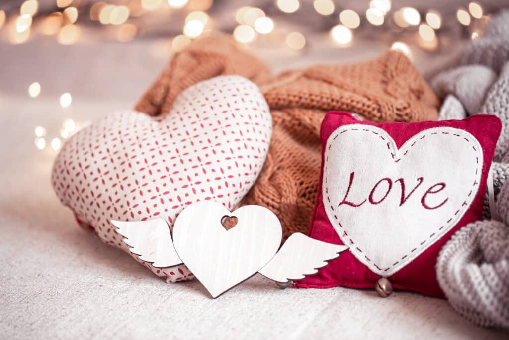 Romantic Valentine's Day setting with cozy heart-shaped pillows and a wooden heart with wings, symbolizing love and warmth.